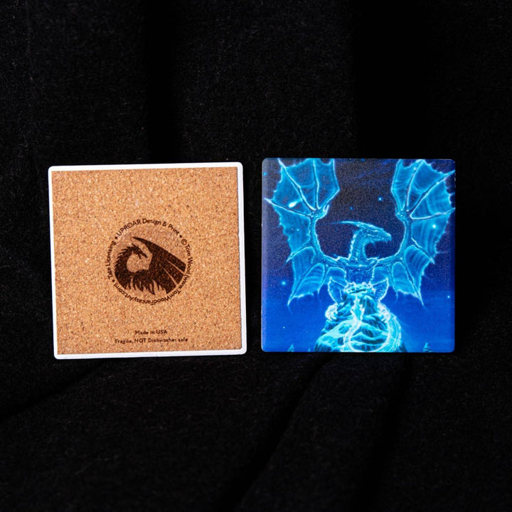 Two square coasters displayed side-by-side on a black fabric background. The coaster on the left is made of natural cork with a printed circular eagle logo and text.