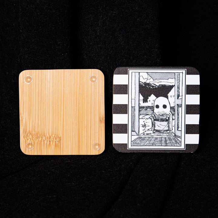 Two square coasters shown side by side on a black fabric background. The left coaster is made of light natural bamboo wood with rounded corners.