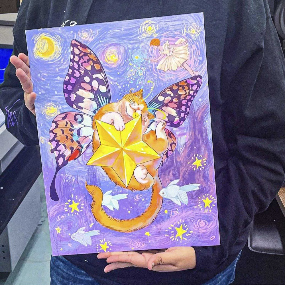 Person holding vibrant custom printed artwork featuring a fairy cat with butterfly wings and glowing star, colorful fantasy art