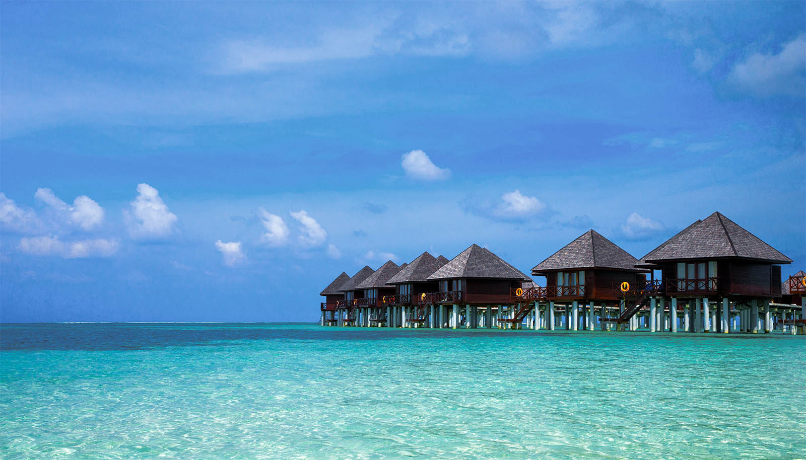 Row of overwater bungalows with clear blue water and sky