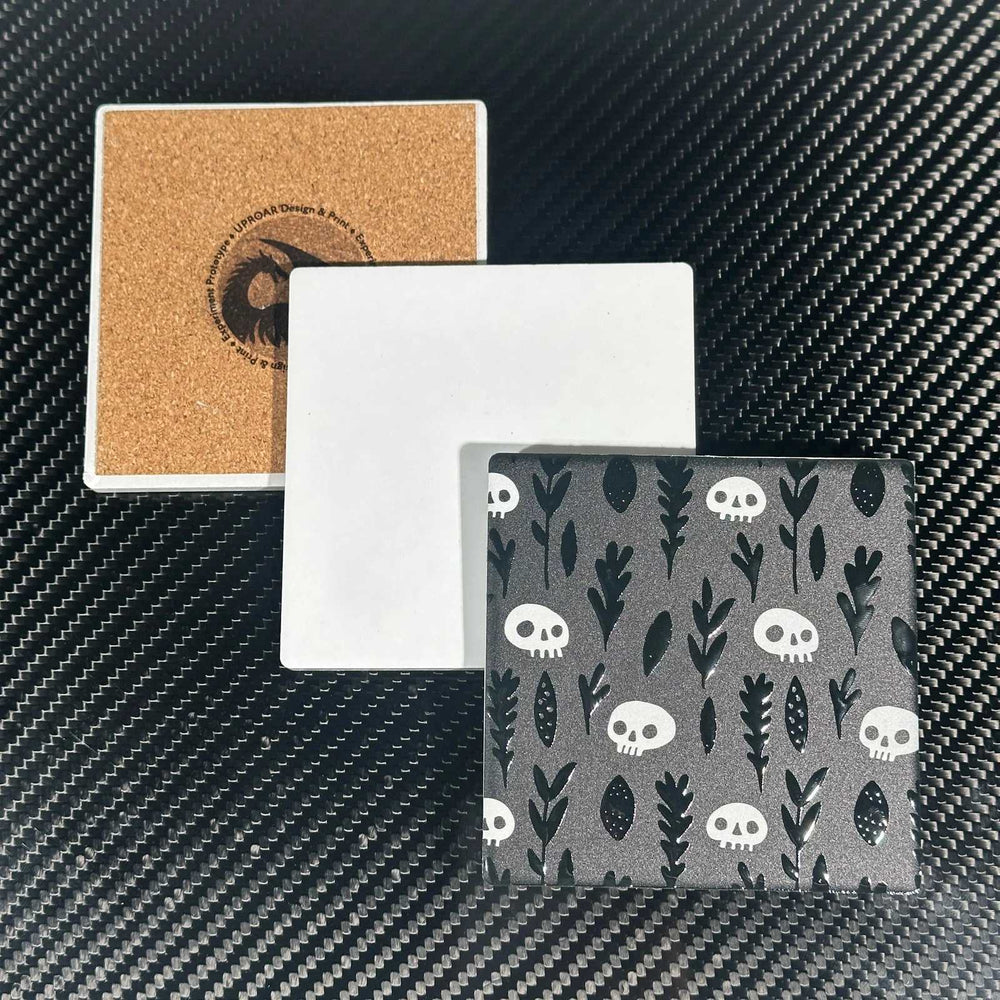 Square coaster samples showing a cork back with the Uproar logo, a blank white face and a printed skull-and-leaf pattern.